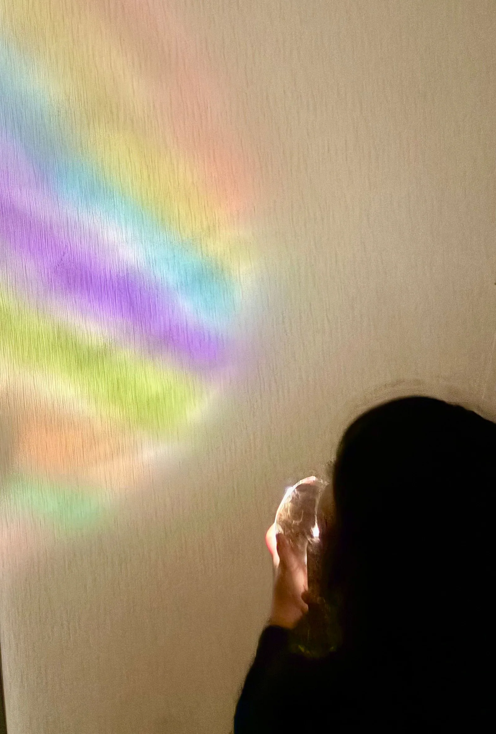 壁に映った虹色の光を見つめる子ども